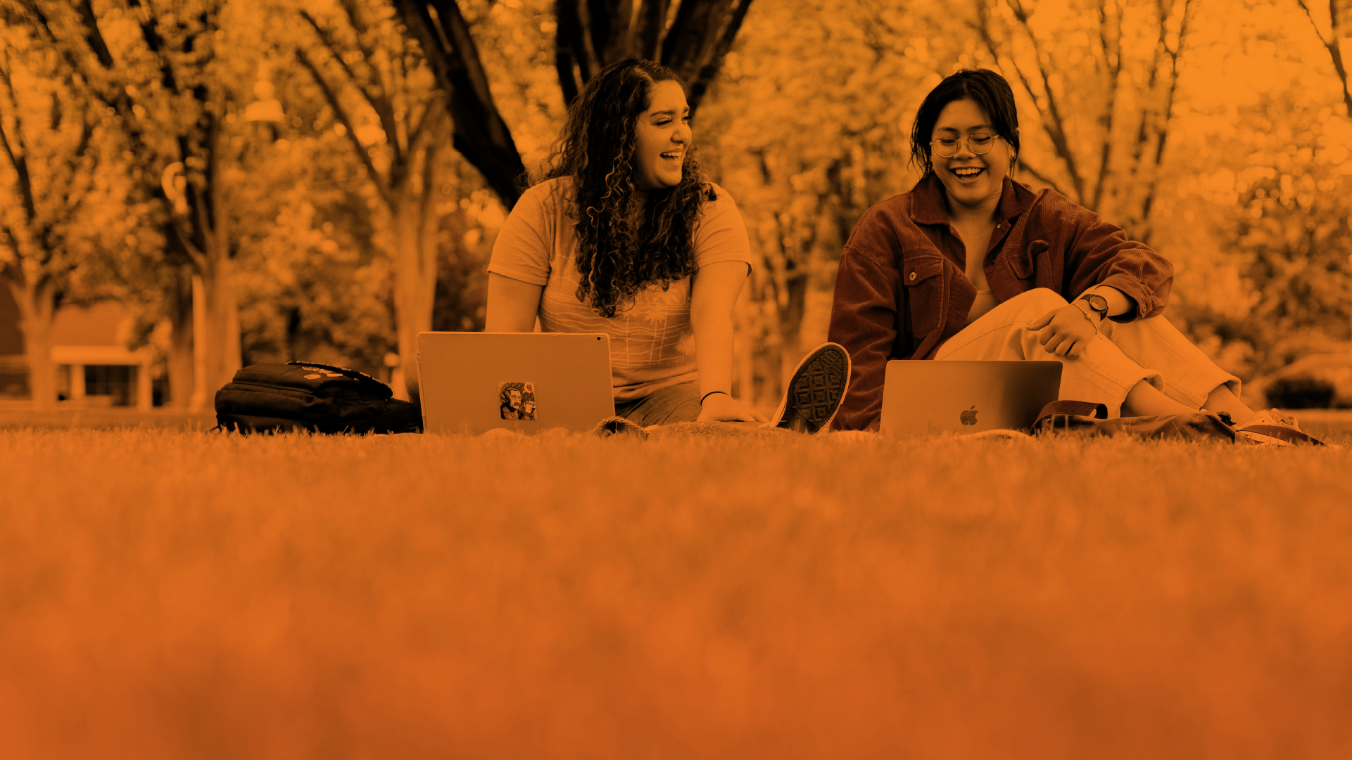 Two students sitting on the grass with laptops