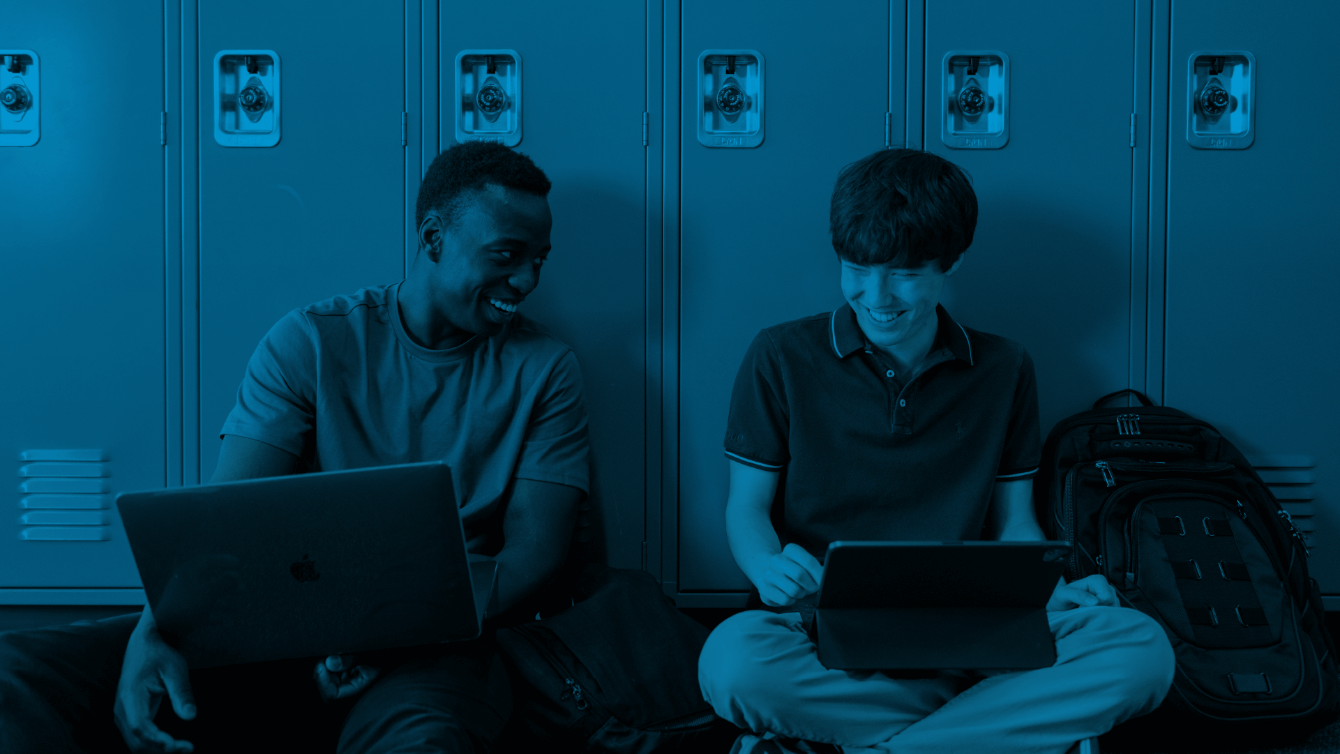 Two male students laughing while opening their laptops