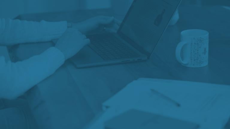 photo of a womans hand on her laptop sitting on her desk by a mug and notepad with a blue overlay