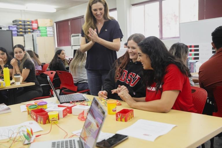 SDSU instructor stands in class with two students viewing a laptop in workshop environment