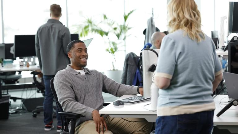 man sitting at computer looking at woman, smiling.