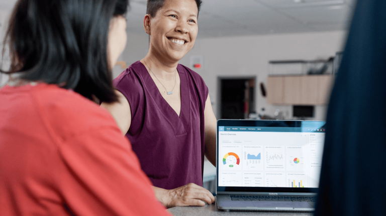 A woman and a man smile at a laptop, sharing a moment of joy and collaboration.